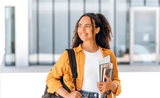 Student wearing backpack 和 smiling holding textbook